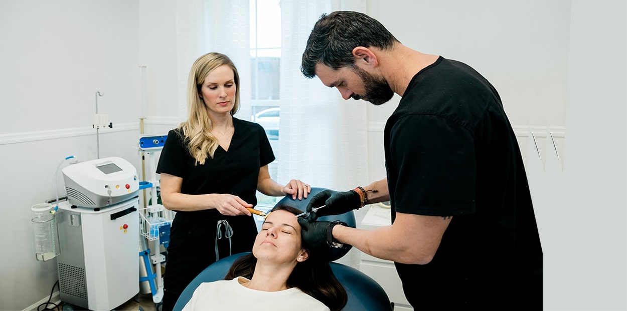 A male and female nurse practitioner treating woman getting botulinum toxin or fillers on her forehead and face.